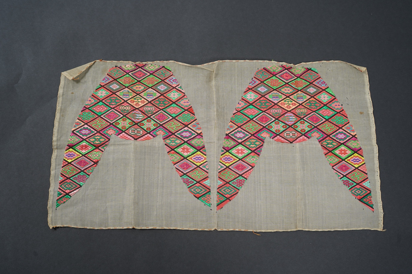 A pair of early 20th century Chinese silk polychrome finely embroidered slipper fronts, possibly from Guangxi province. Embroidered in a diamond grid, with stylistic and symbolic motifs. 21.5cm top to base. Condition - u